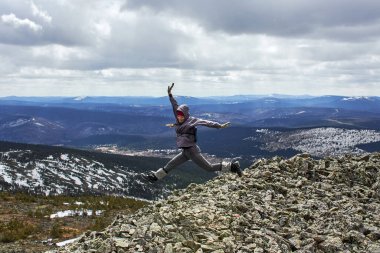 Kadın bir dağın tepesinde kollarını kaldırarak atlıyor, doğal çevrede ve yaşam tarzında özgürlük ve neşe ifade ediyor. Argydzhek Dağı 'nın tepesinde.