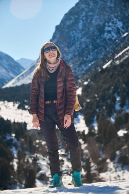 Kar dağında yürüyüş yapan bir kadın, mutlu bir gülümsemeyle yukarı bakıyor. Doğada kış yolculuğu macerası. Açık hava aktivitesi.