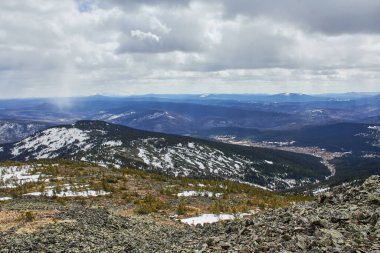 Karla kaplı yamaçlı dağ manzarası ve bulutlu bir gökyüzünün altında seyrek ağaçlar. Seyahat ve macera konsepti için manzara doğa görünümü.
