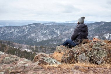 Kayaya oturmuş, kış manzarasına bakan bir kadın. Seyahat ve açık hava macerası için dinginlik ve tefekkür kavramı. Sahne doğa görünümü arkaplanı.