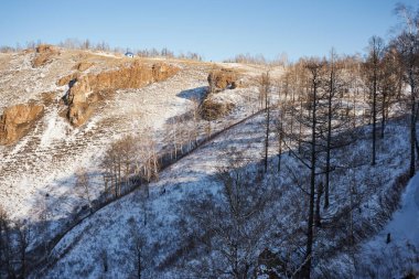 Üstünde çıplak ağaçlar ve küçük bir ev olan güzel karlı bir tepe manzarası. Seyahat ve çevre konsepti için mavi gökyüzü olan kış manzarası.