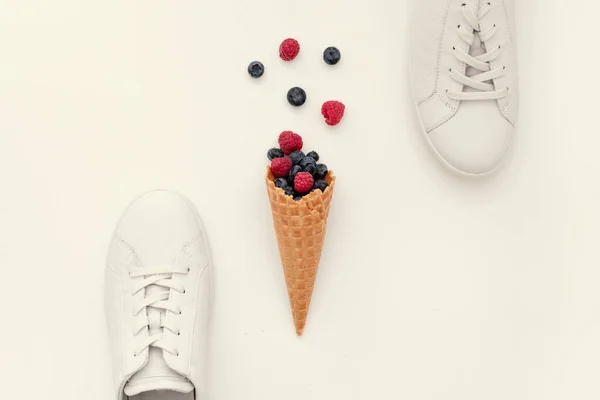 White women\'s sneakers and a horn with summer berries on a light background, close-up, minimal, art, modern. The concept is the enjoyment of quality shoes. Flat lay, top view