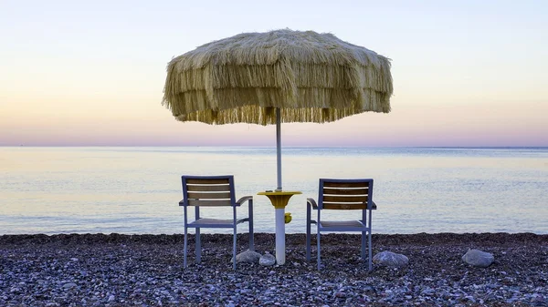 Two empty chairs stand on beach under open umbrella overlooking — Stock Photo, Image