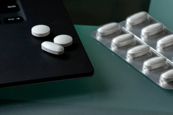 The package of tablets is next to the laptop. Several tablets are lying on the edge of the laptop. The laptop image is cut off. Selective focus.