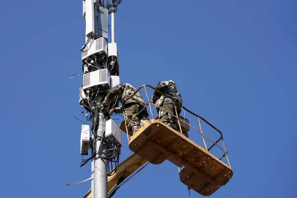 Installation of cellular equipment on the tower. Two communications engineers work at altitude from a lifting cradle. Copy space.
