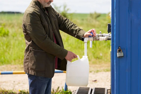 A man draws water from the water intake well\'s flow tank into a plastic container.