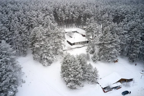 Aerial view of a lonely house with a courtyard, located in the middle of a snow-covered forest. Snow is falling.