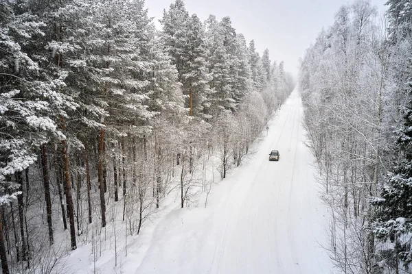 Winter road in the forest with a lone passenger car. Shooting from a drone.