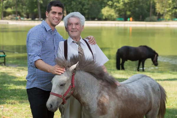 Grandfather and grandchild stroking pony — Stock Photo, Image