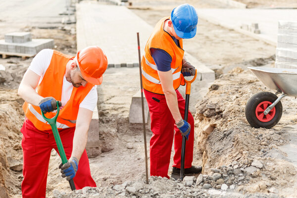 Рабочие засыпают песок в тележку
