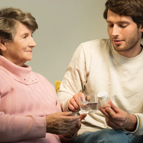 Hombre joven dando medicamentos abuela — Foto de Stock