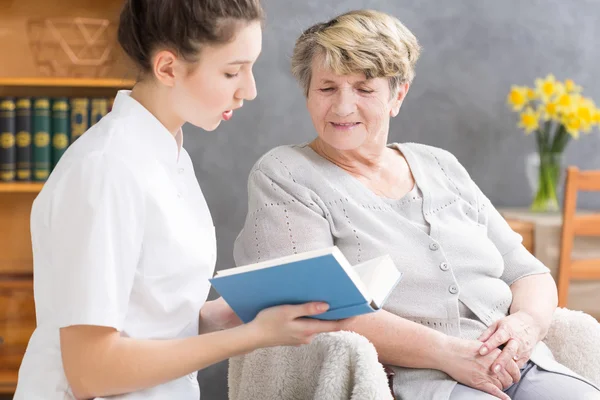 Betreuerin liest Seniorin vor — Stockfoto