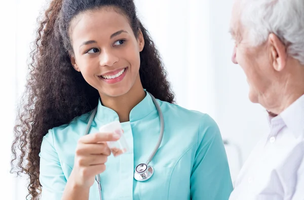 Smiling female caregiver giving senior man pills — Stock Photo, Image