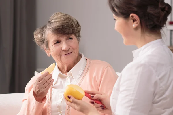 Літня жінка і доглядальниця їдять яблуко — стокове фото