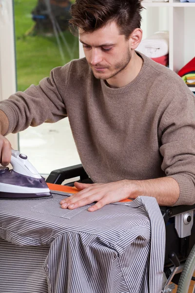 Mann im Rollstuhl bügelt Hemd — Stockfoto