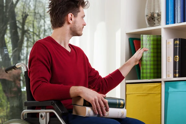 Disabled man cleanig up a bookshelf — Stock Photo, Image