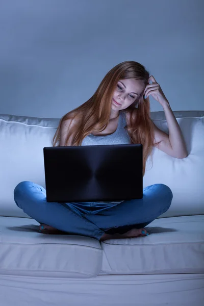 Девушка сидит на диване и с помощью компьютера — стоковое фото