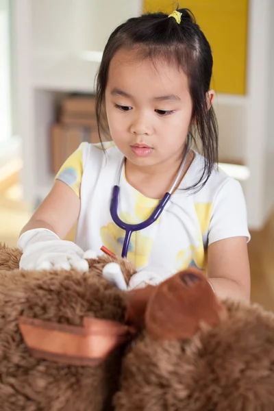 Asian girl examining teddy bear — Stock Photo, Image