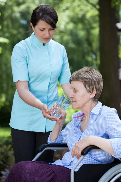 Vårdgivare ger glas vatten till äldre kvinna — Stockfoto