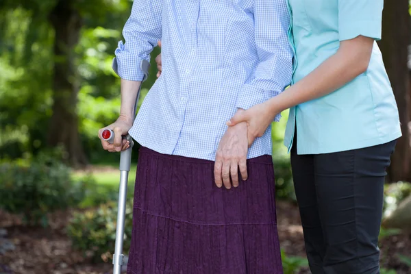 Verpleegkundige wandelen met een vrouwelijke patiënt met een kruk — Stockfoto