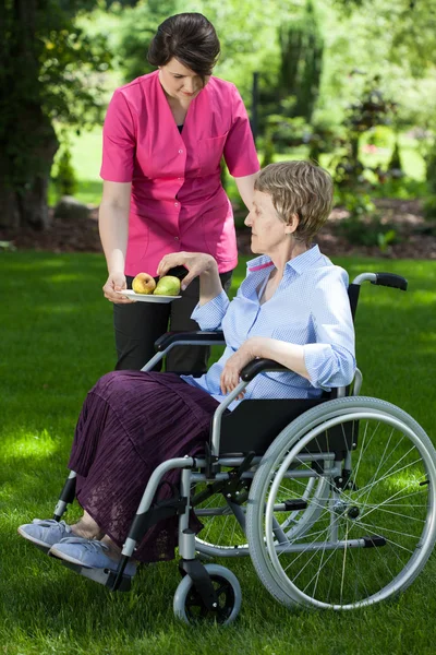 Cuidador dando pêra a mulher idosa com deficiência — Fotografia de Stock
