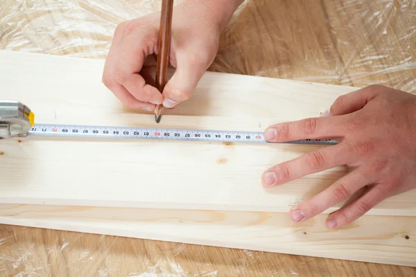 Hands measuring wooden plank with measuring tape and pencil — Stock Photo, Image