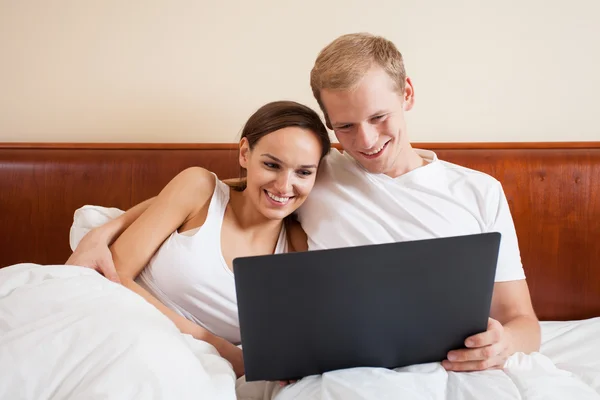 Pareja feliz en la cama con portátil — Foto de Stock