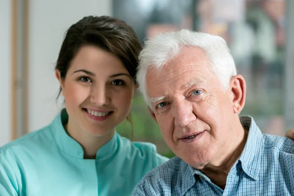 Sorridente uomo anziano e giovane infermiera — Foto Stock