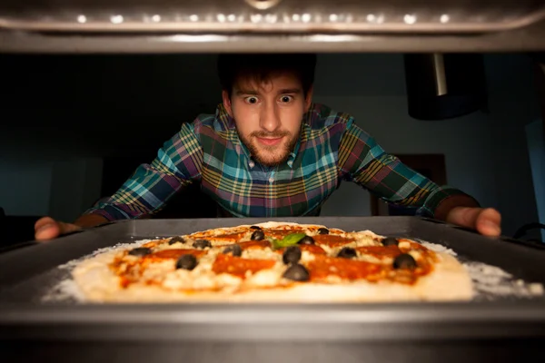 Человек берет пиццу из духовки — стоковое фото