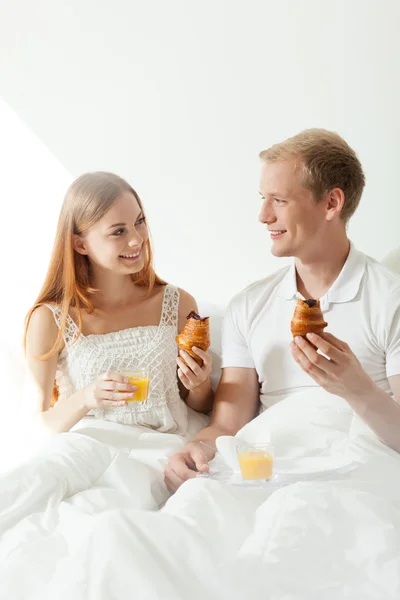 Pár jíst croissanty v posteli — Stock fotografie