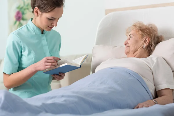 Verzorger zieke patiënt boek lezen — Stockfoto