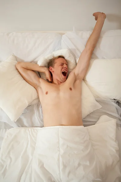 Человек просыпается и зевает в постели — стоковое фото