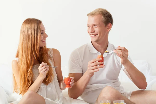 Hombre y mujer comiendo huevos en la cama — Foto de Stock