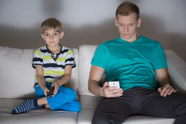 Dítě sleduje televizi a táta pomocí telefonu — Stock fotografie