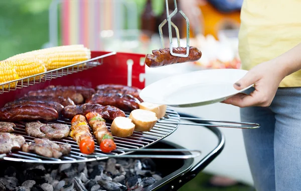 Woman dishing out grilled sausages — Stock Photo, Image