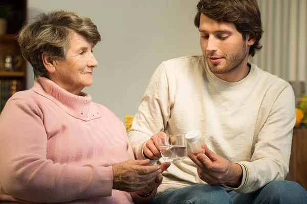 Young man giving grandmother medicament — Stock Photo, Image