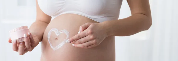 Беременная женщина наносит крем — стоковое фото