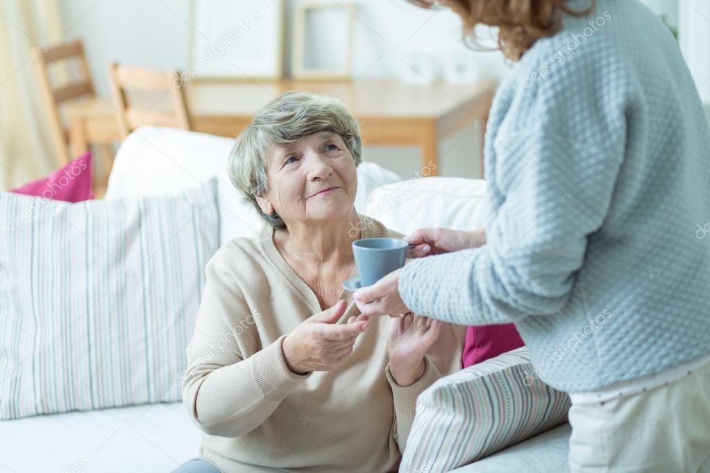 Caregiver giving elder woman coffee