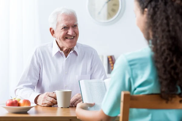 Pensionär och sjuksköterska läser bok — Stockfoto