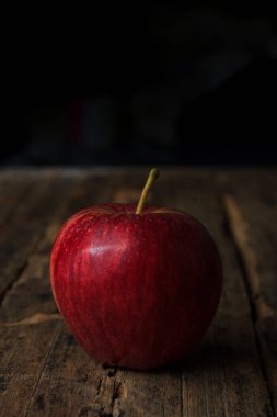Koyu renklerle süslenmiş eski ahşap bir masada kırmızı elmalar..