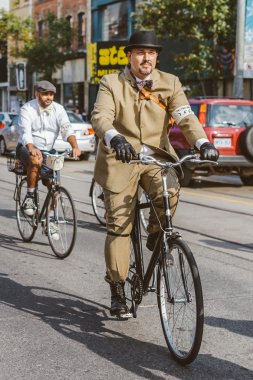 Toronto, Canada - September 20, 2014: Unidentified participants of Tweed Ride Toronto in vintage style clothes riding on their bicycles. This event is dedicated to the style of old England clipart