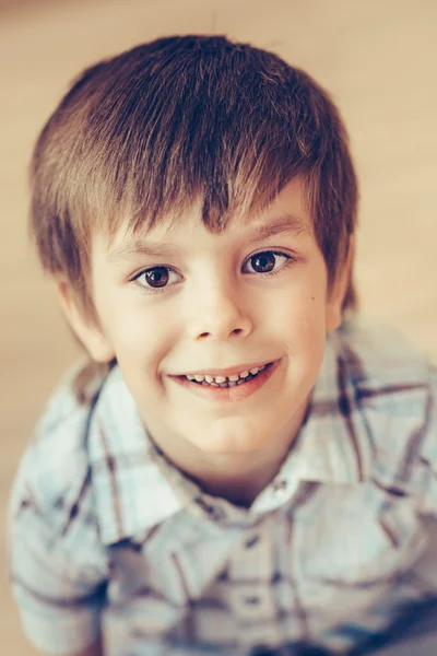 Closeup portrait of cute smiling little boy with brown eyes wearing checkered shirt sitting on floor and looking at camera. Happy childhood concept, selective focus on eyes, top view, instagram filter — Stock Photo, Image