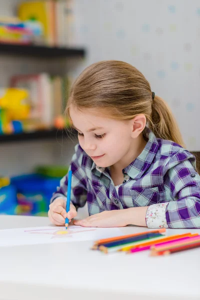 Linda niña sonriente con el pelo rubio sentado en la mesa blanca y dibujo con lápices multicolores — Foto de Stock