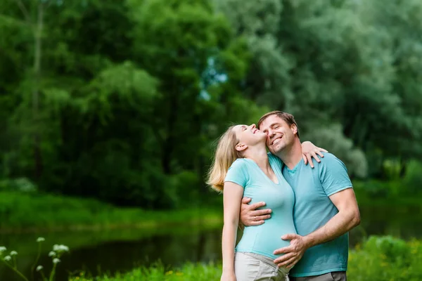 Un bell'uomo sorridente che abbraccia la sua bella giovane donna incinta e le tocca la pancia nel parco estivo. Concetto di famiglia felice e gravidanza. Festa della mamma — Foto Stock
