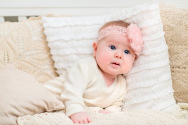 Güzel kız bebek örgü yastıklar ile yatakta yatarken çiçekli beyaz giysiler ve pembe bant giyen büyük mavi gözleri ve tombul yanakları şaşırttı. Şişmesi ve çocukluk kavramı