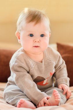 Sevimli küçük çocuk ile sarı saçları ve Mavi giyen örme kazak kanepede oturan ve bacağını dokunmadan gözler. Mutlu çocukluk