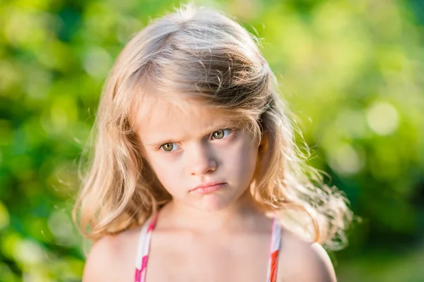 Close-up portrait of capricious blond little girl with pursed lips. Sunny summer day in beautiful park — Stock Photo, Image