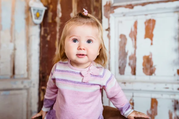 Amazed funny blond little girl with big grey eyes and plump cheeks looks up. Studio portrait on grunge background — Stock Photo, Image