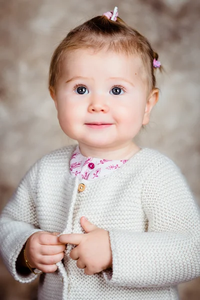 Close-up portrait of beautiful blond little girl with big grey eyes and plump cheeks keeping her finger in her hand. Studio portrait on grunge background — Stock Photo, Image