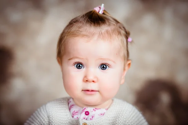 Retrato de una niña rubia sonriente con grandes ojos grises y mejillas gordas. Retrato de estudio sobre fondo grunge marrón —  Fotos de Stock